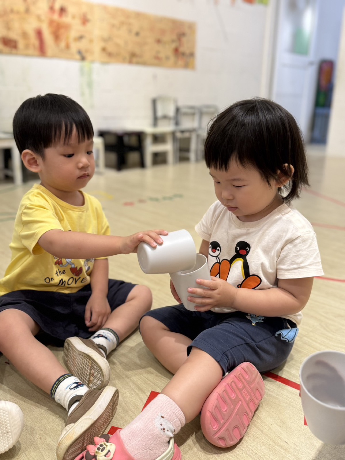 兩位孩子練習將杯子中的物品倒入另一個杯子